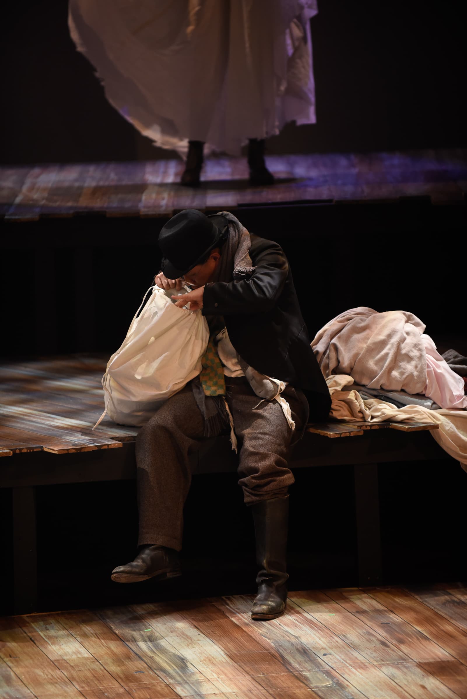 A man is on staged and dressed in turn of the century clothing and peering into a bag with unknown contents.