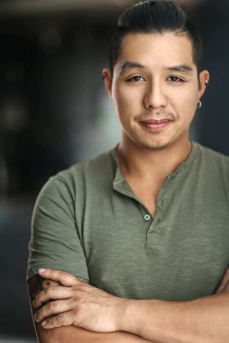 Aerhyn Lau standing with his arms cross and smiling with one eyebrow raised.