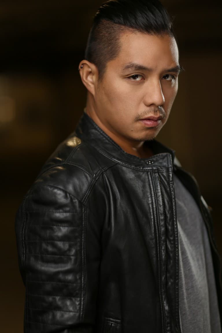 Aerhyn wearing a black leather jacket and looking at the camera. His body is facing sideways.