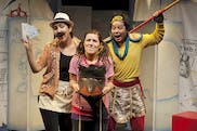 Three people look like they're about to head out on a safari. One person is wearing a tribal mask, another is holding tickets, and a third is wearing a tiger-patterend loin cloth over his clothes. There ae backdrops with maps on them behind the people.